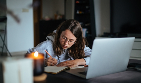 Female student writing by laptop