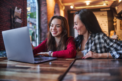 Mother and daughter smiling while using the laptop together.